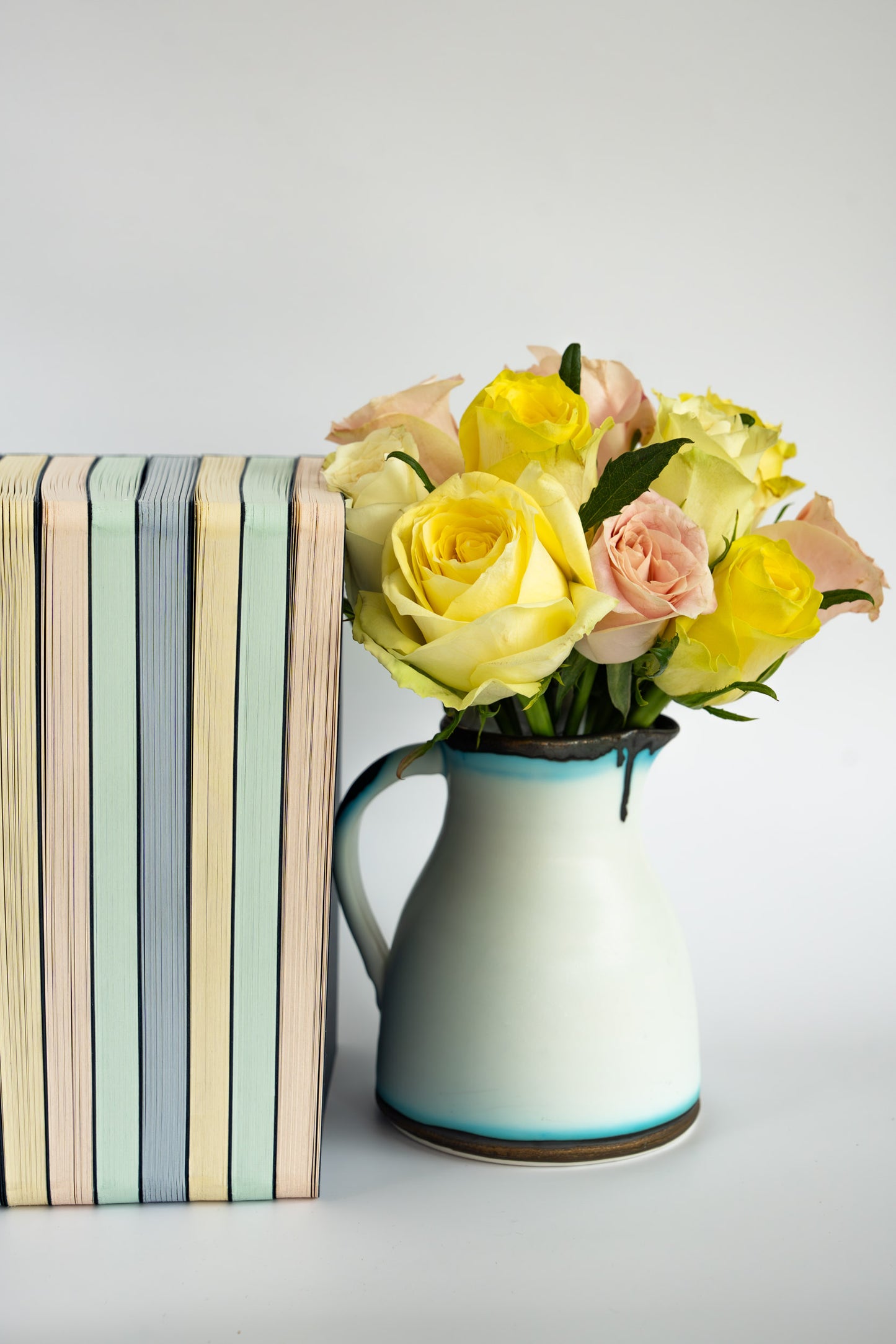 Vase with yellow and pink flowers next to a stack of The OakBook of all colours